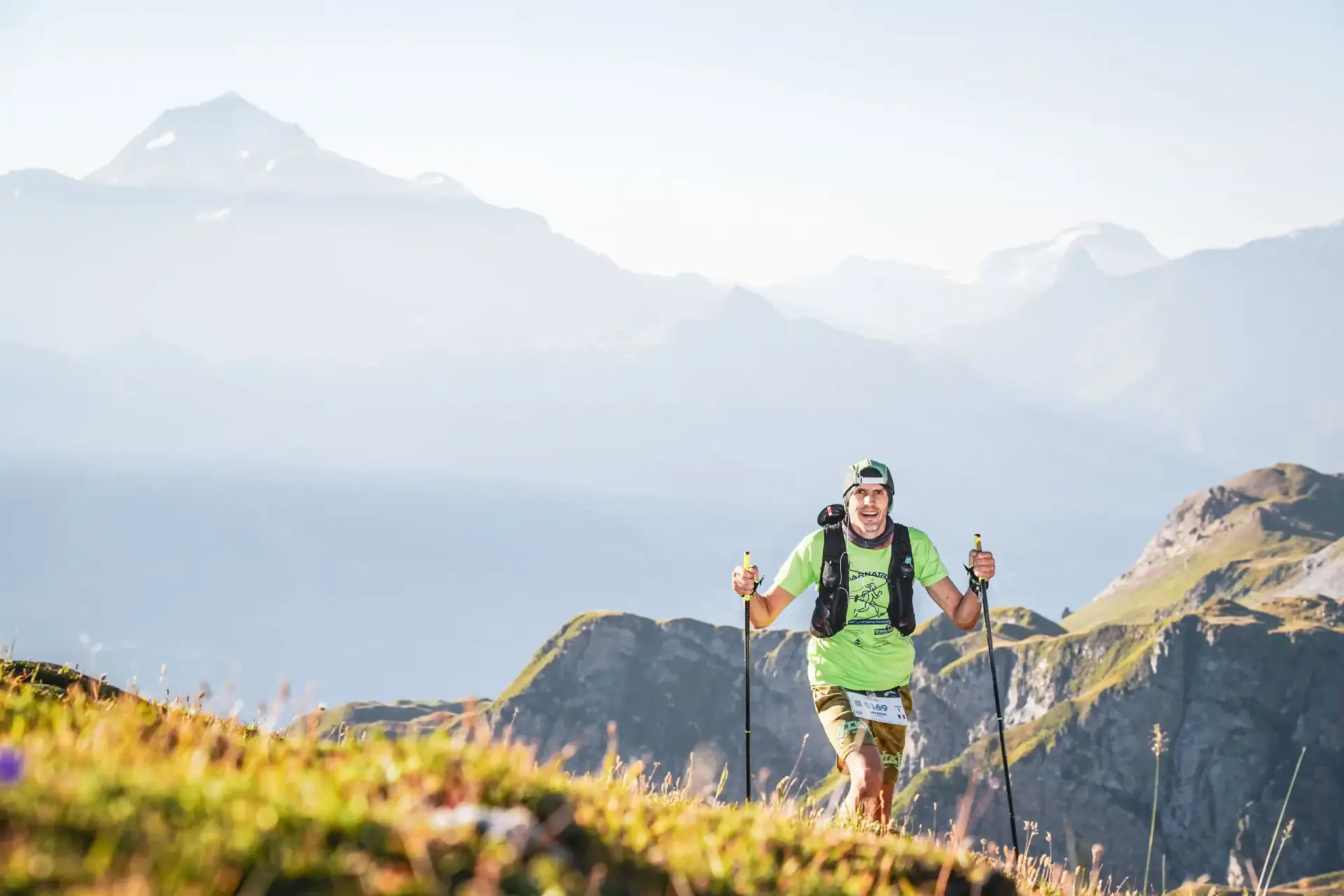 Trail runner souriant en plein état de flow courante dans un paysage de montagne ensoleillé, illustrant le plaisir et la performance mentale.